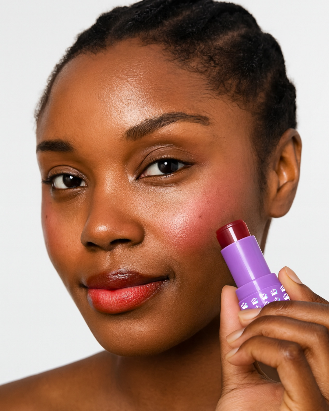 Model holding an open tube of Mo-Beauty Shop's Mo-Jelly Blush + Lip Tint stick in the shade Chili Crisp, showing the buildable red color applied on lips and cheeks, on a white background