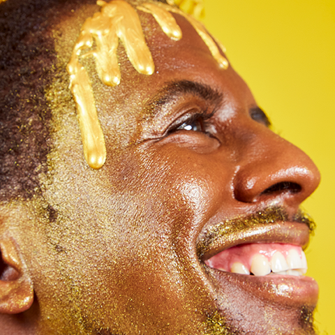 Model dripping in Mo-Beauty Shop's Gimme Mo-Glow All-Over Highlighter in the Gold shade.